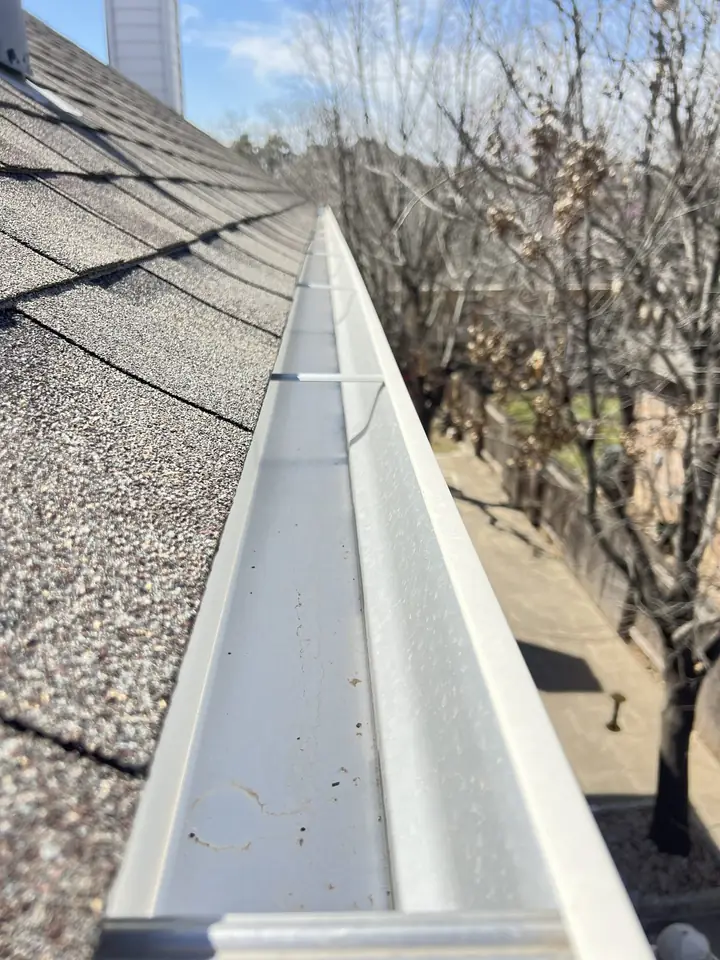 Freshly cleaned gutter along a shingle roofline with trees behind the house