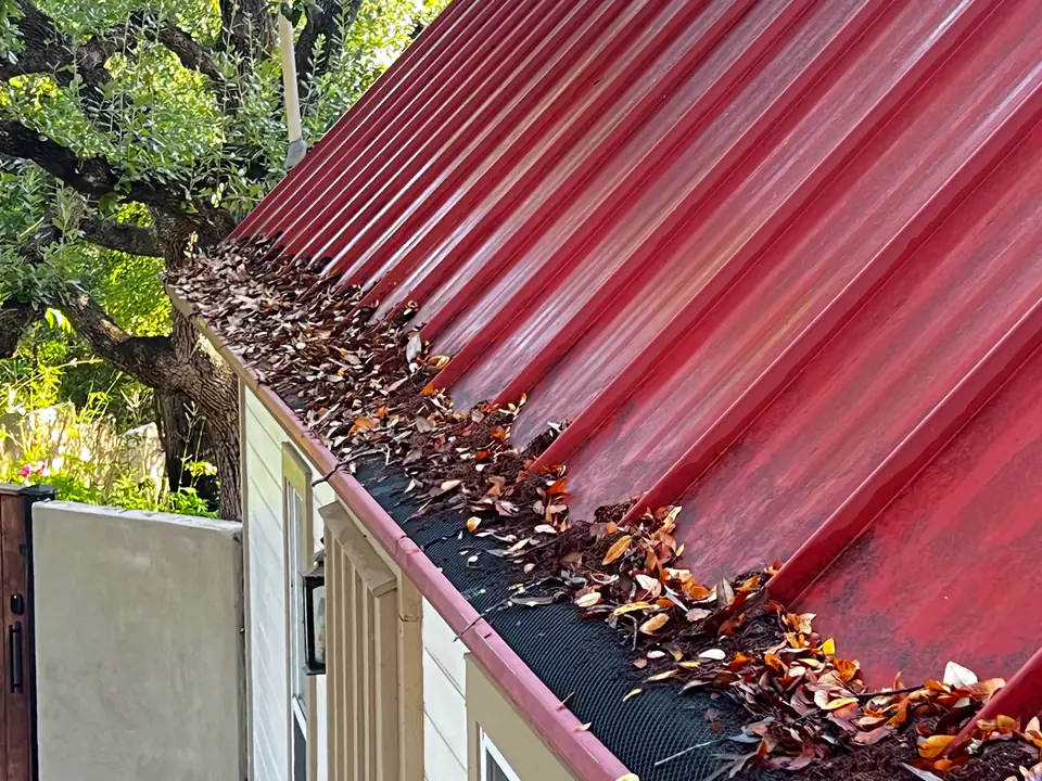 Leaves piled on top of gutter guards along a red metal roof before a Casa Care cleaning