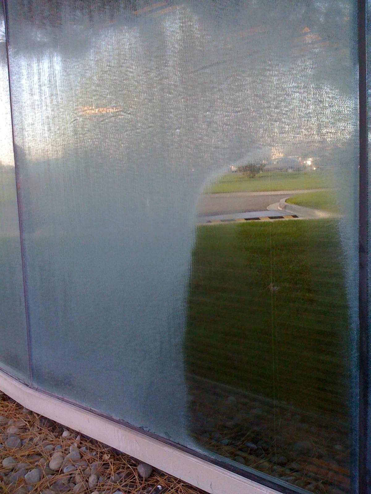 Window glass clouded with heavy hard-water mineral buildup, with one test section cleaned clear to show the view through