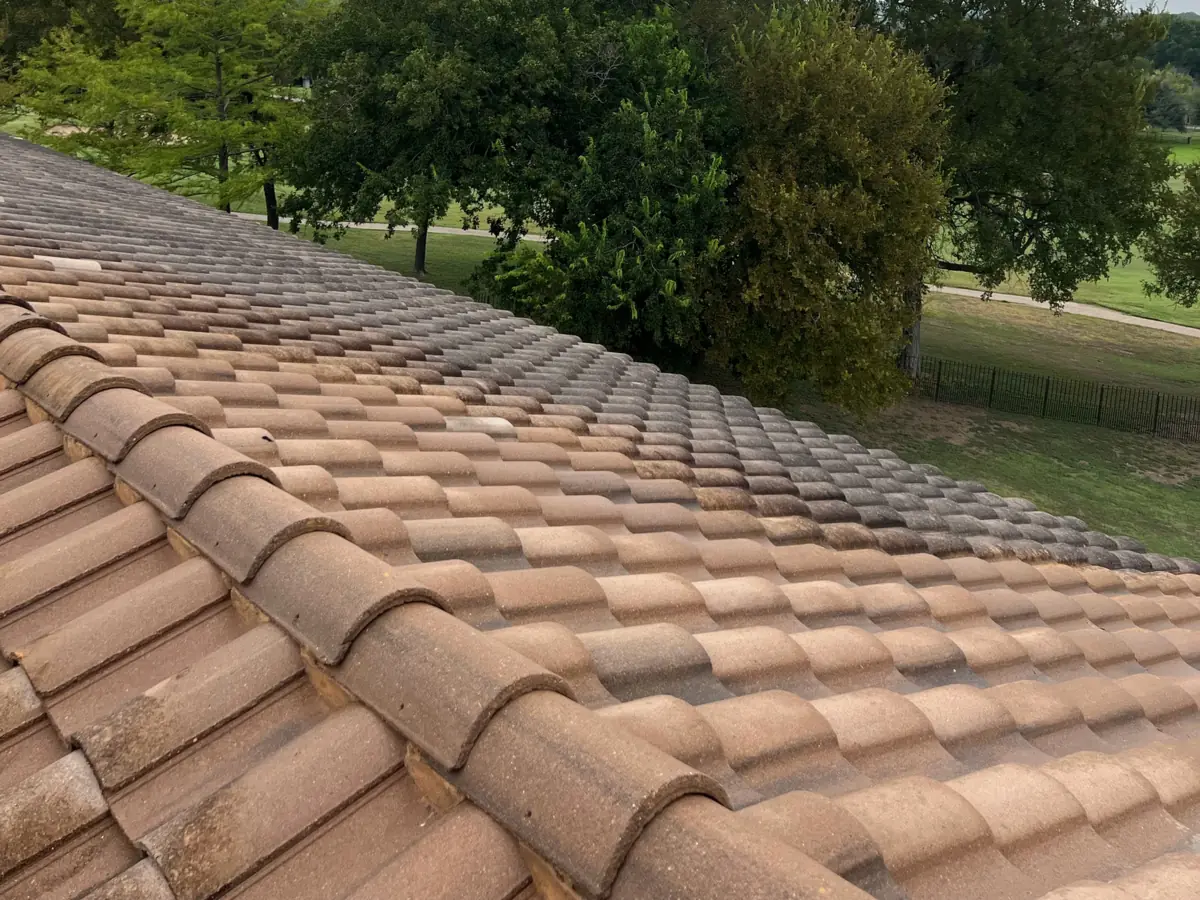 Tile roof partway through a Casa Care soft wash, nearer tiles cleaned to an even terracotta and farther rows still gray and stained