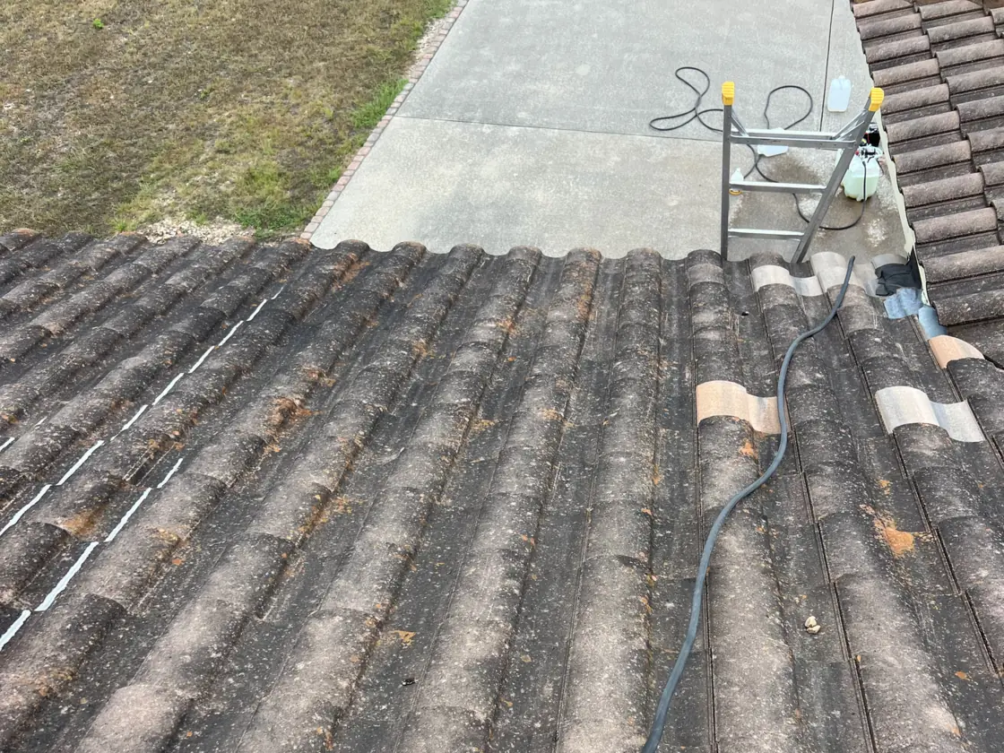 Casa Care soft wash setup on a stained concrete tile roof, a hose running across dark streaked tiles to a ladder and pump sprayer at the eave