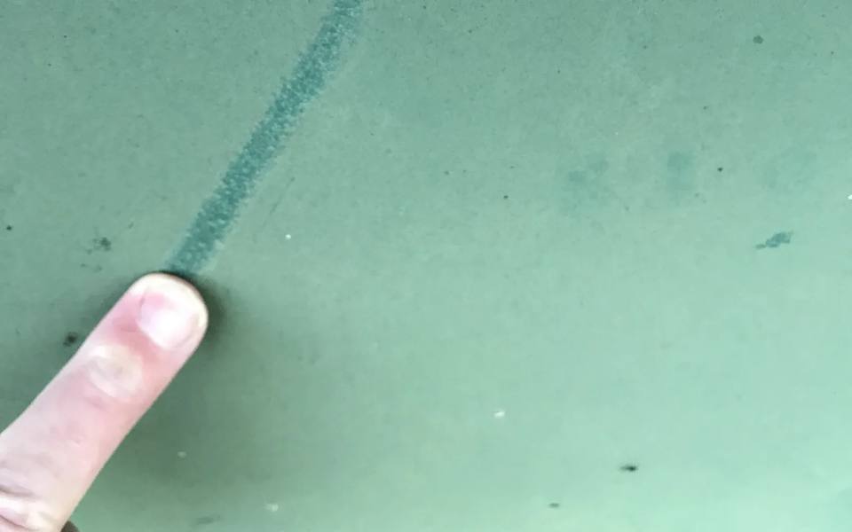 Finger wiping a chalky oxidized green painted surface, revealing darker paint underneath